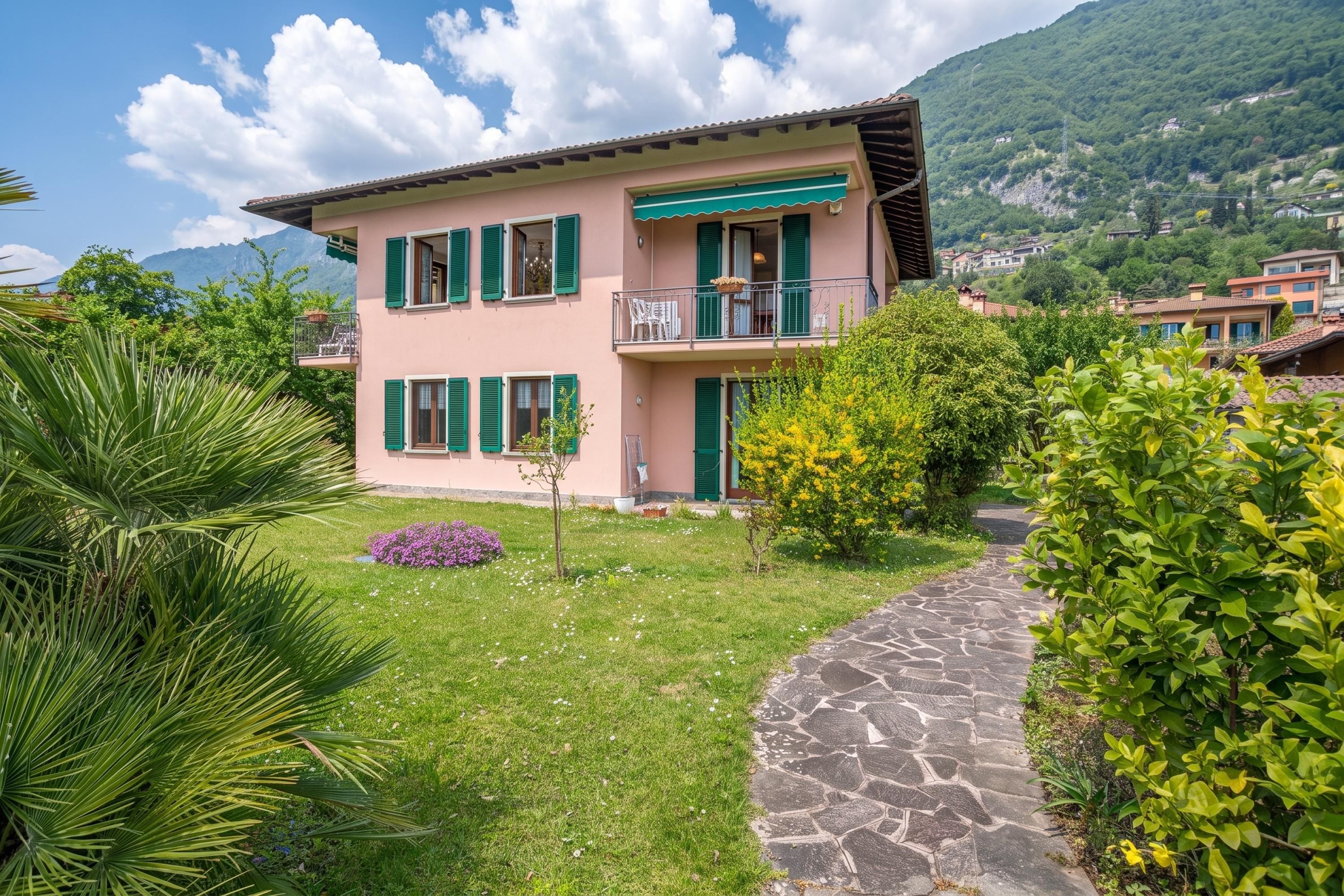 A two-story house with a stone pathway leading to the entrance, surrounded by greenery and a mountain backdrop.