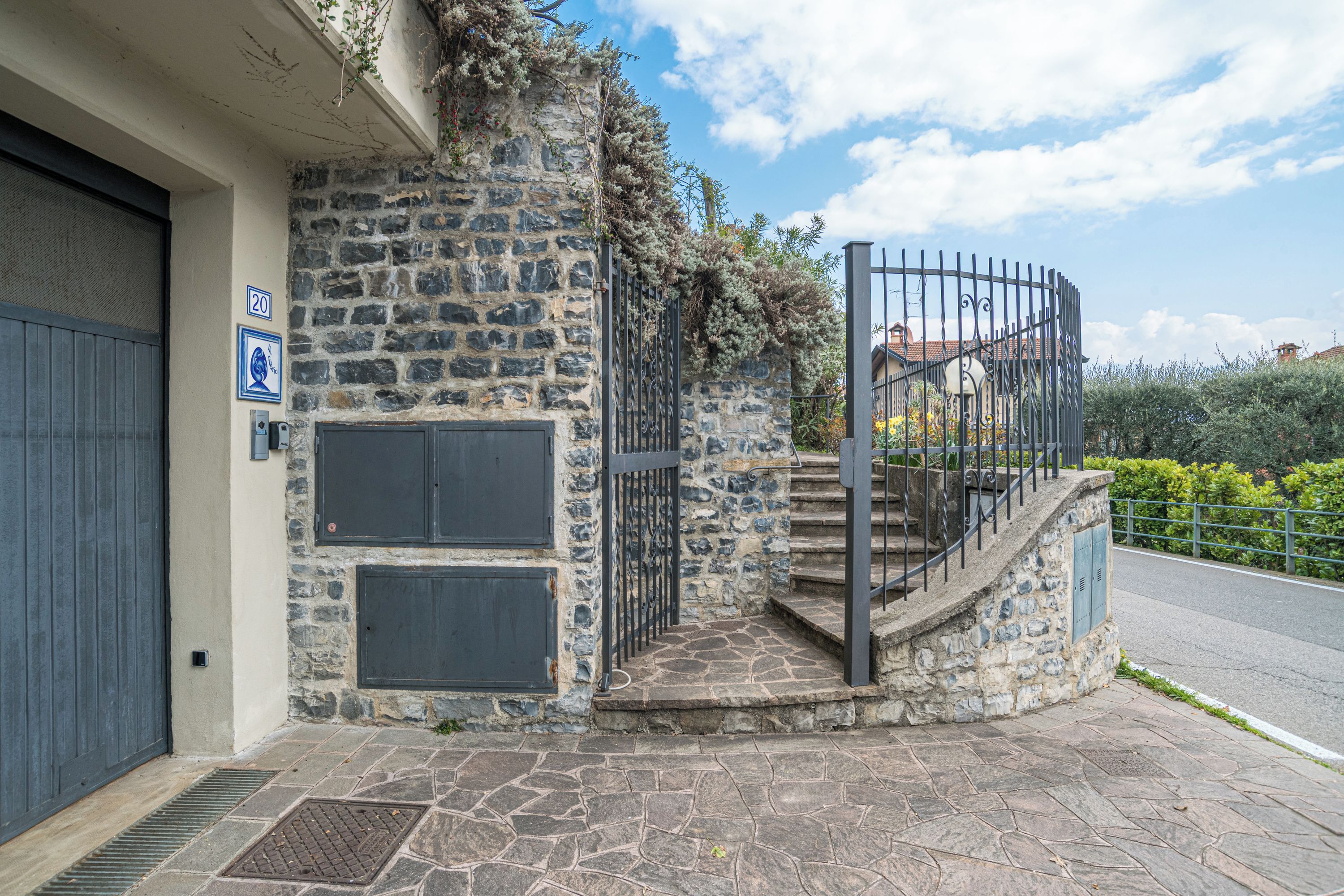 A stone building with a metal staircase, a garage door, and a blue sign with a white symbol.