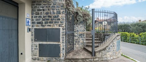 Um edifício de pedra com escadas de metal, uma porta de garagem e uma placa azul com um símbolo branco.
