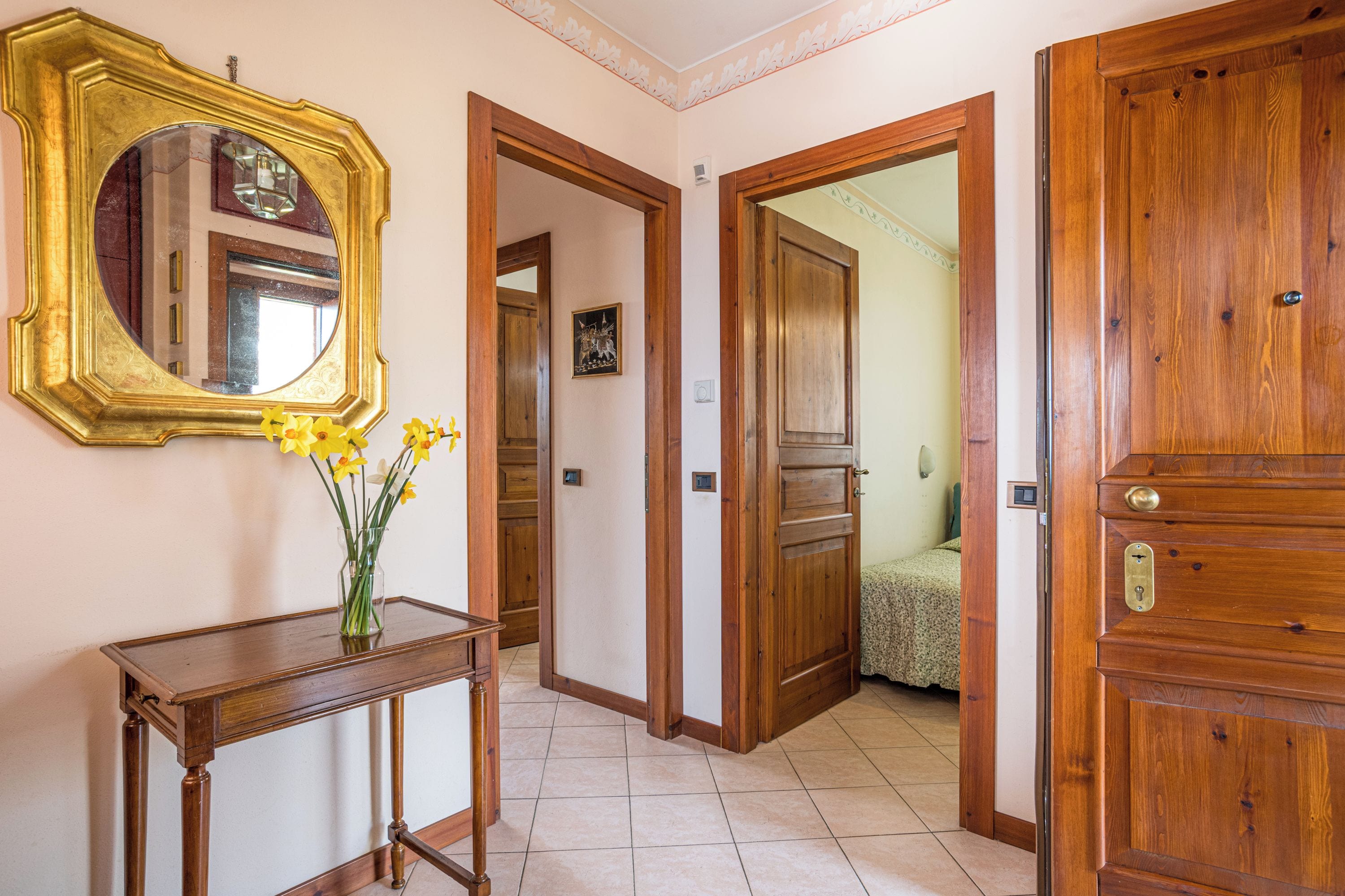 Un couloir avec une porte en bois, un miroir et un vase rempli de fleurs.