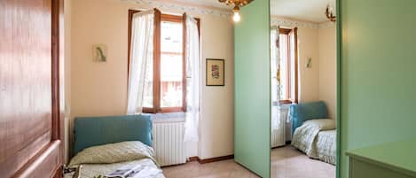 Un dormitorio con una cama, una ventana con cortinas, un radiador, un espejo y una araña.