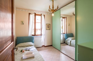 Um quarto com cama, janela com cortinas, radiador, espelho e lustre.