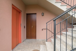 Uma escada com corrimãos de metal, uma porta de madeira e um candeeiro fixo na parede.