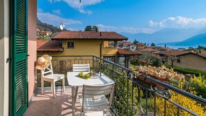 A balcony with a table and chairs, a view of houses and mountains, and a clear sky. - Lenno Il Guscio (Tremezzina)