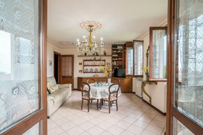 Uma sala de jantar com um candelabro, uma mesa posta para quatro pessoas e um sofá ao fundo.
