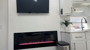 Moderni keittiö, jossa on litteänäyttöinen televisio, sisäänrakennettu takka, valkoiset keittiökaapit ja ikkuna, josta on kaunis näkymä.