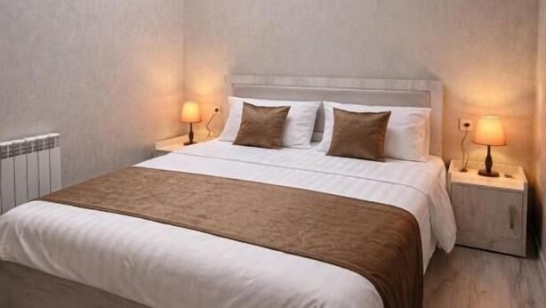 A bedroom with a skylight, a bed with white and brown bedding, two bedside lamps, and a radiator. - Urban nest old Tbilisi (Tbilisi)