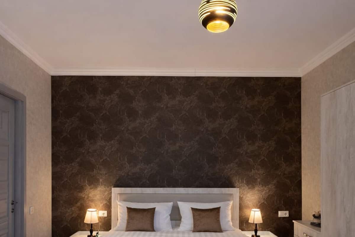 Un dormitorio con una cama grande, dos lámparas de noche, una lámpara colgante moderna y una pared con estampado de mármol.
