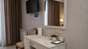 A hotel room with a wooden desk, a television mounted on the wall, a chair, a small trash bin, and slippers on the floor. - Urban nest old Tbilisi (Tbilisi)