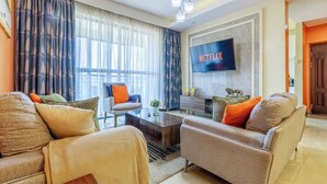 A living room with a sofa set, a coffee table, a TV mounted on the wall, and a decorative lion statue. - 3-bedroom apartment in wonderful Nairobi with indoor pool and garden (Nairobi)