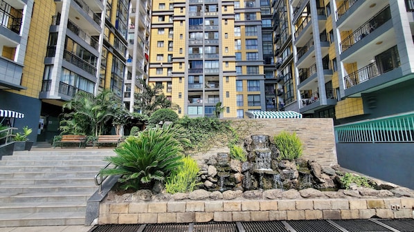 A multi-story residential building with balconies, a small waterfall feature, and a staircase leading to the entrance.