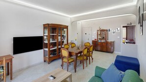 A living room with a dining table, chairs, a sofa, a TV, and a bookshelf. - Apartment 'Le Stelle Di Zia Pina' with Sea View, Wi-Fi and Air Conditioning (Torre del Greco)