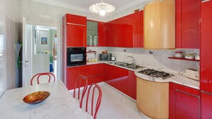A modern kitchen with red cabinets, a marble countertop, a gas stove, and a dining area with a bowl and chairs. - Apartment 'Le Stelle Di Zia Pina' with Sea View, Wi-Fi and Air Conditioning (Torre del Greco)