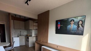 Ein modernes Zimmer mit Bett, Schreibtisch, Wand-Fernseher und einer Küchenzeile im Hintergrund.