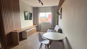 Ein modernes Wohnzimmer mit einem runden Esstisch, zwei weißen St ühlen, einer Couch, einer hölzernen Bank und einem großen Fenster mit Vorhängen.