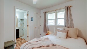 A bedroom with a bed, a bedside table, a window with curtains, a door, and a hallway leading to a bathroom. - 5 Mi to Elephant Rocks State Park Condo (Ironton)