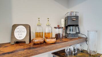 A coffee bar setup with a sign, coffee dispensers, a coffee maker, and mugs.