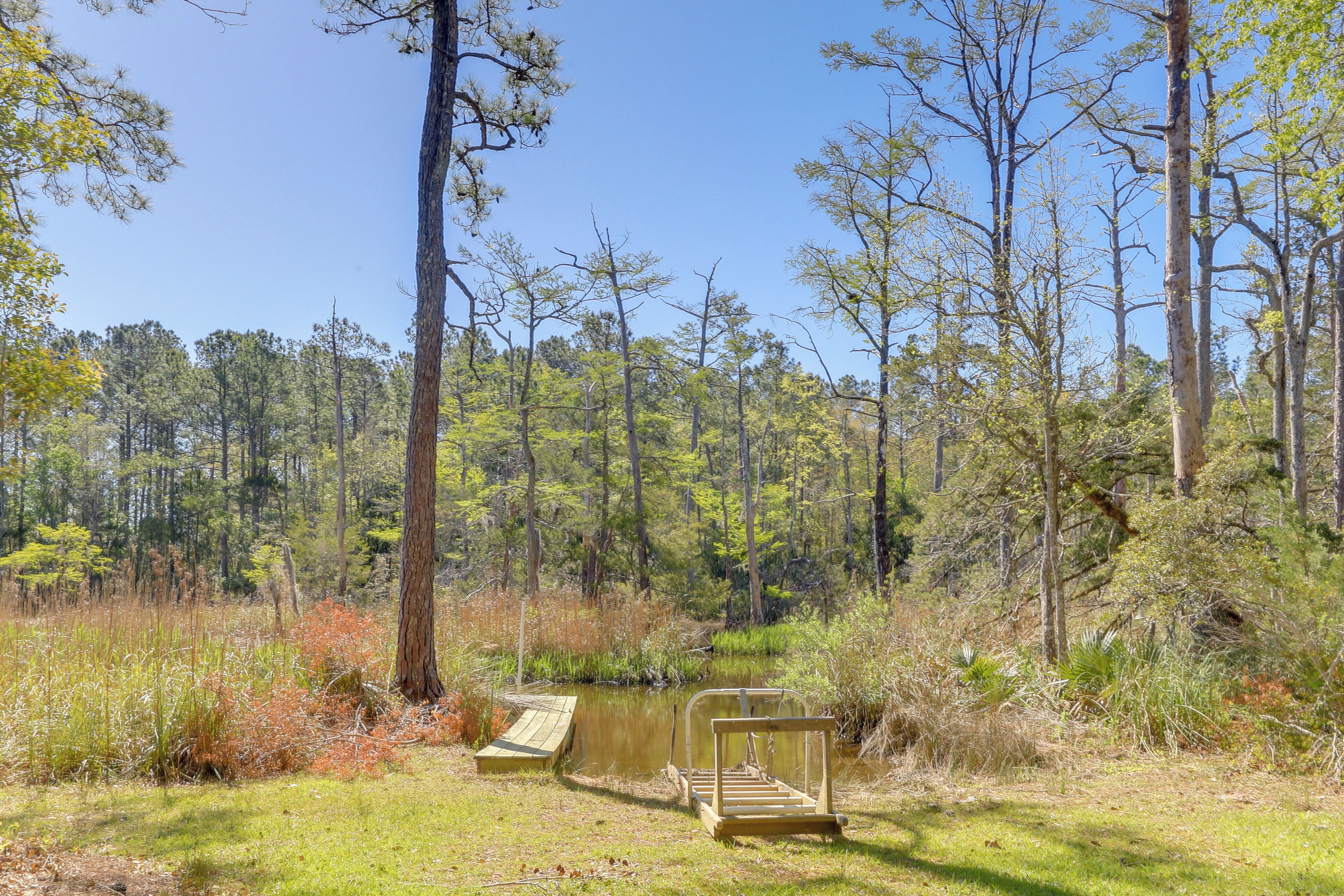 A natural setting with a wooden bench and a small dock by a calm body of water surrounded by trees.