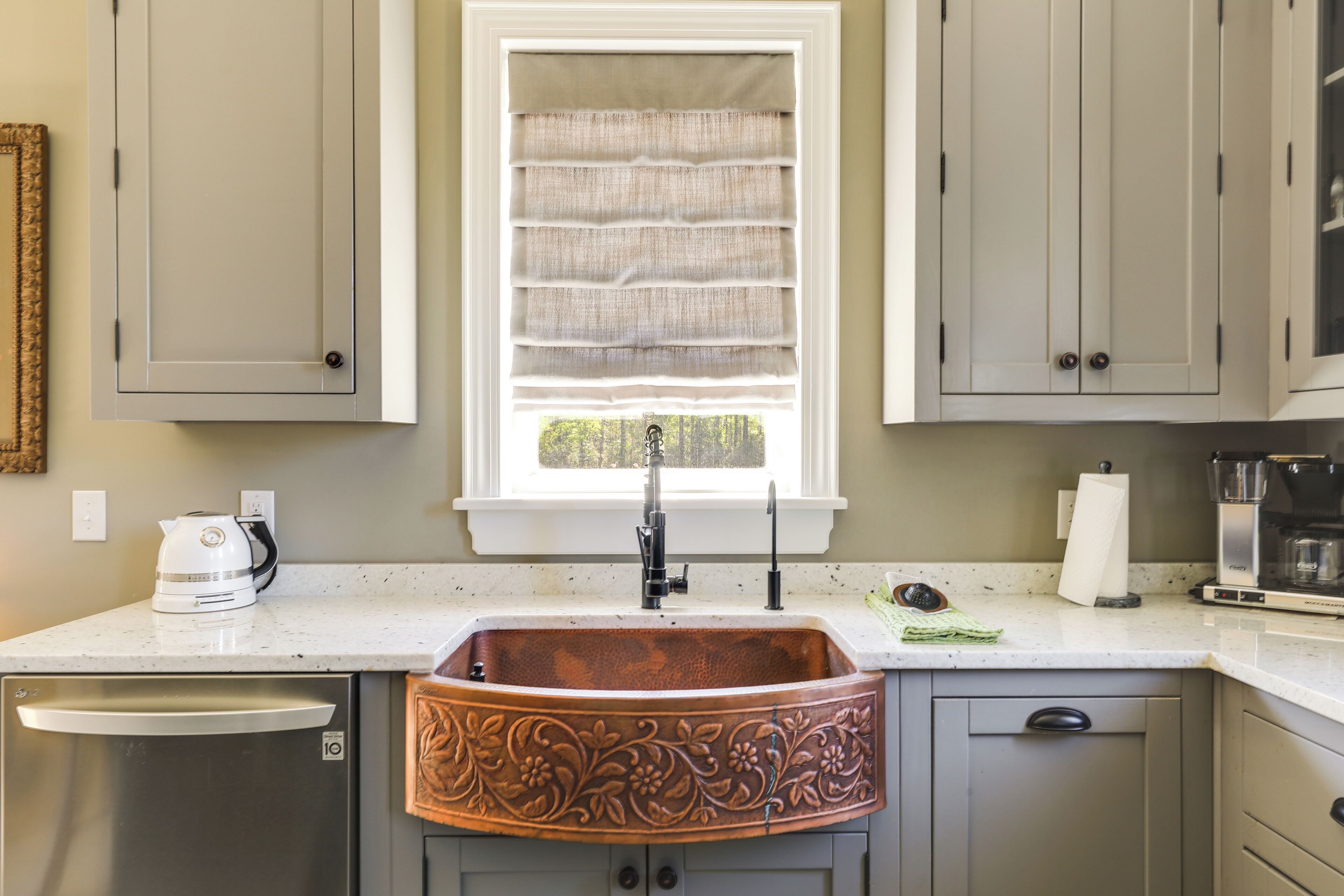A kitchen with a copper sink, a window with blinds, and a coffee maker.