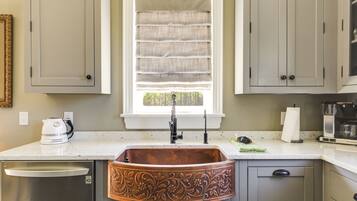 A kitchen with a copper sink, a window with blinds, and a coffee maker.