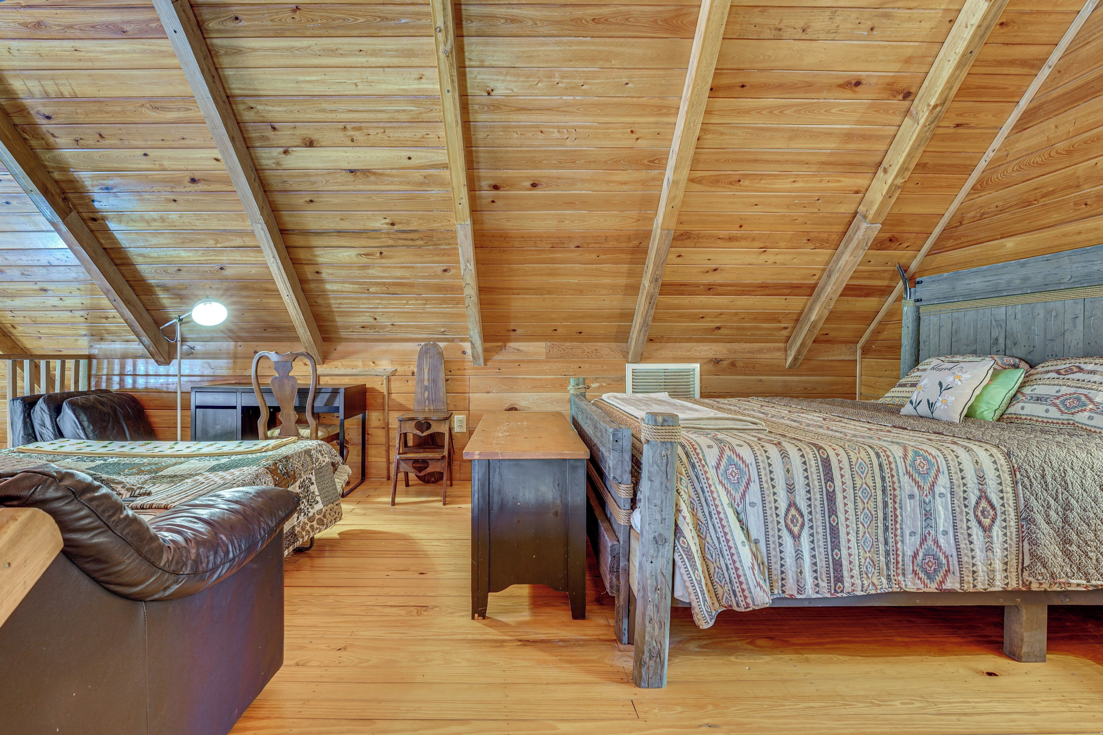 A cabin with a wooden ceiling, a bed with patterned bedding, a desk, and a chair.