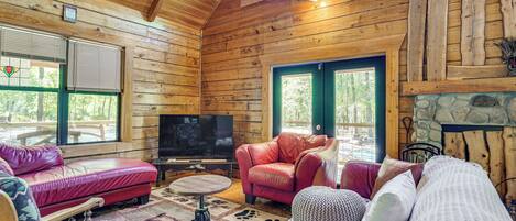 A log cabin interior with a fireplace, leather sofas, a television, and a stone wall.