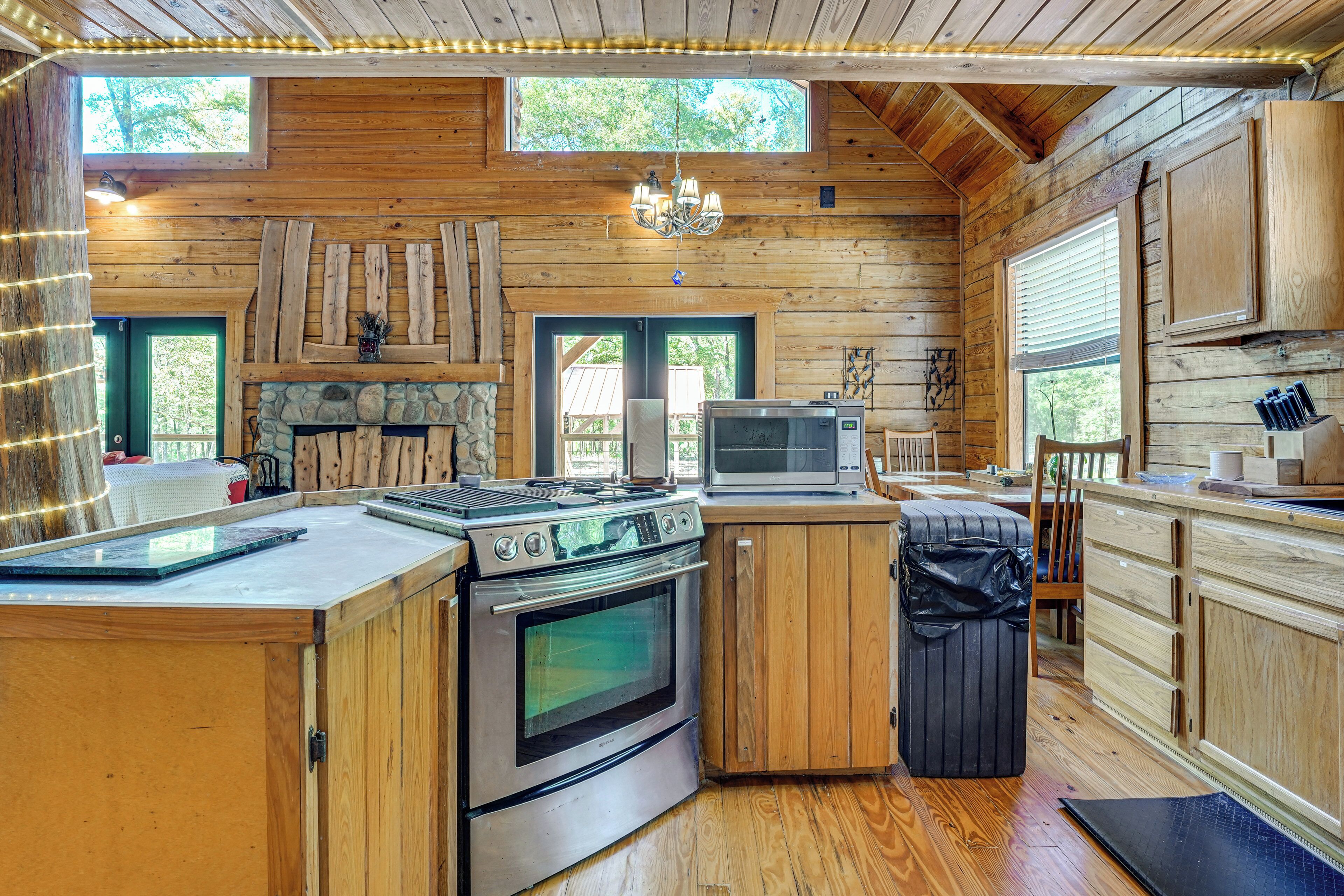L’intérieur d’une cabane comprend une cheminée en pierre, des armoires en bois, un poêle, un four à micro-ondes et une grande fenêtre.