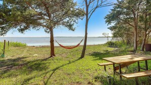 A picnic table and hammock by a lake with trees and grass.