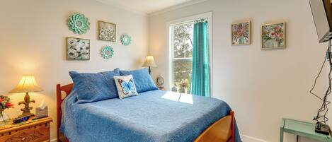 A bedroom with a bed, bedside table, lamp, wall art, and a window with curtains.