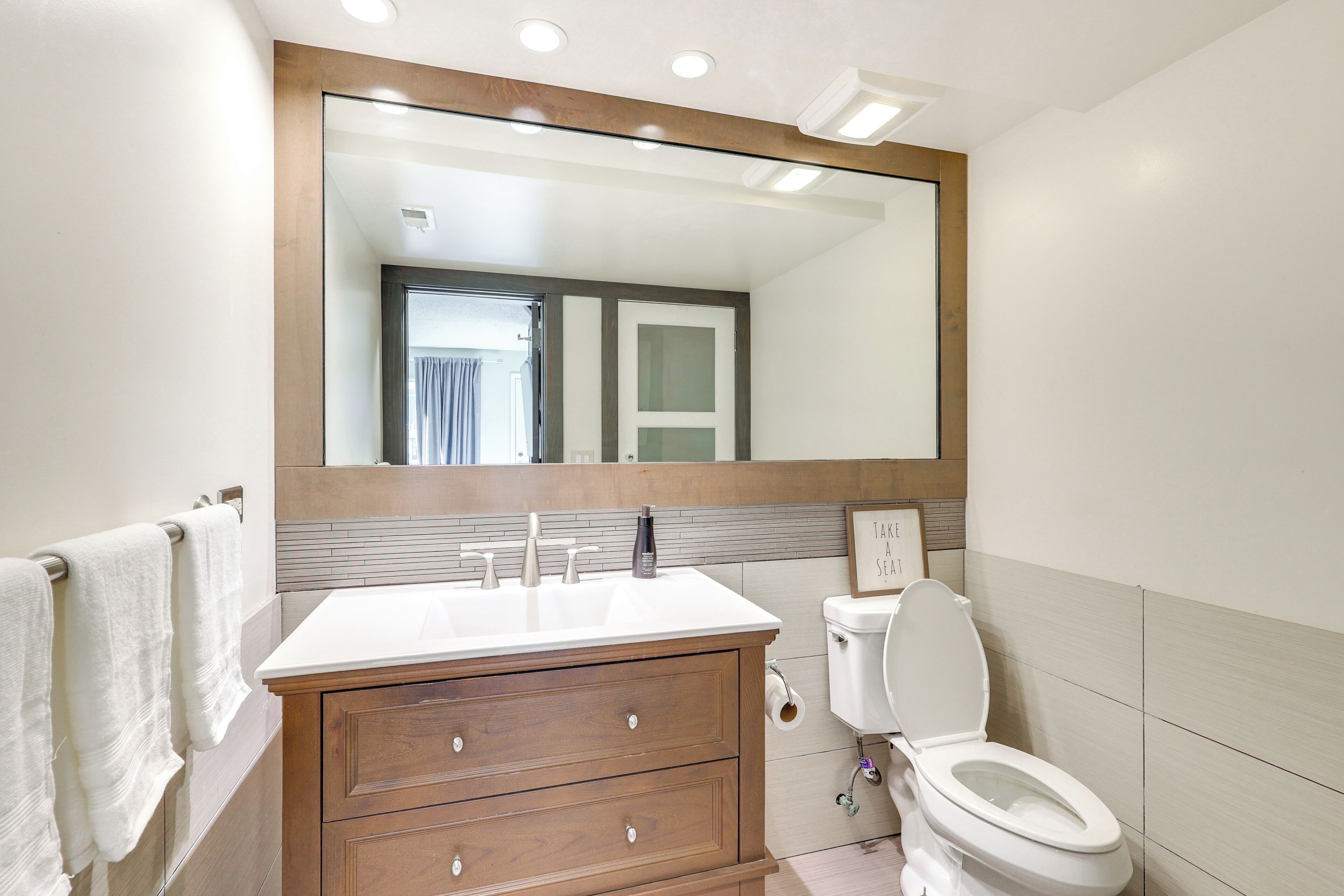 A modern bathroom with a white sink, wooden vanity, and a toilet.