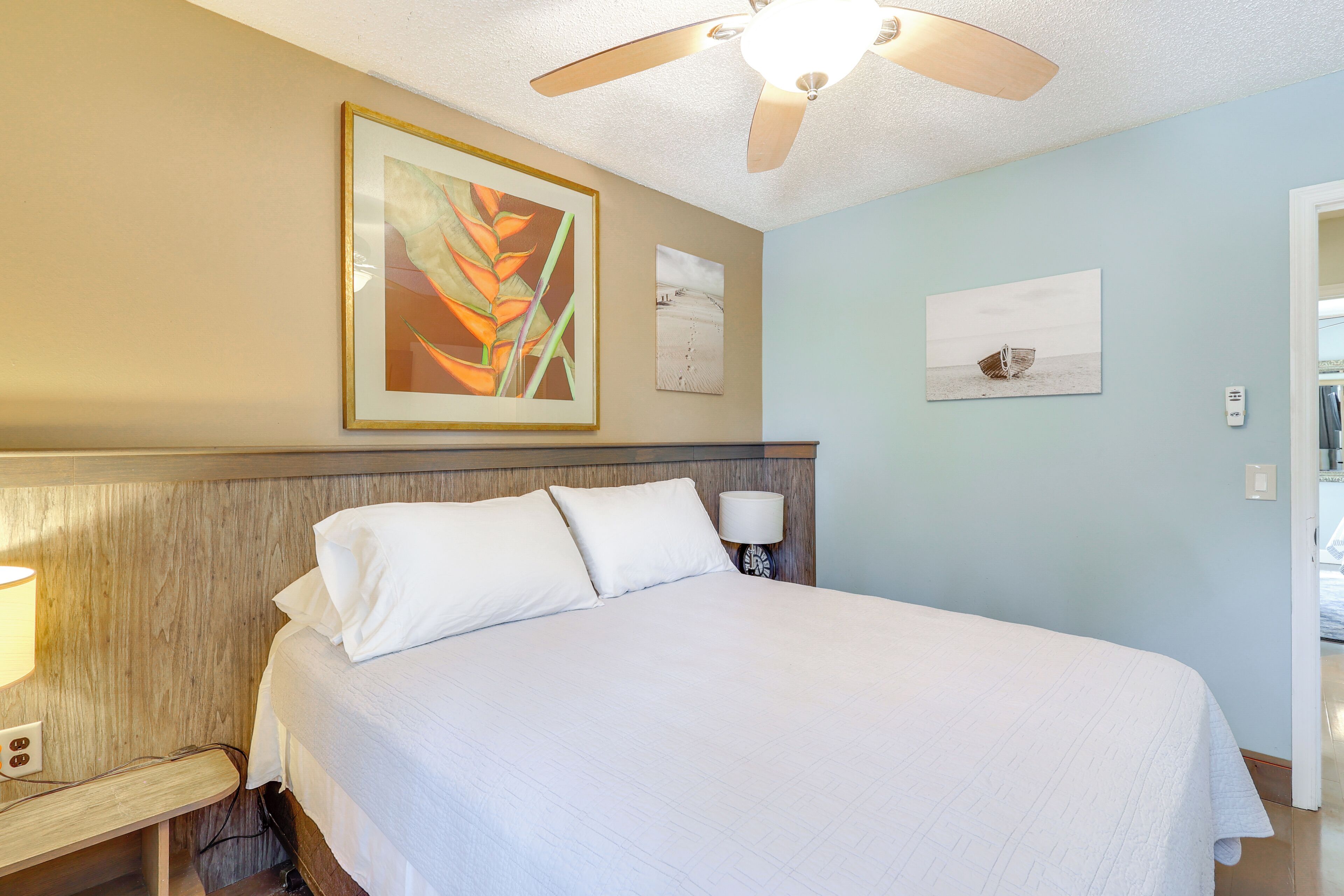 A neatly made bed with white linens, a wooden headboard, and a ceiling fan.