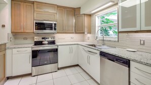 A modern kitchen with wooden cabinets, stainless steel appliances, and a window with a view of greenery. - Water View! Walkable Gem Near Bayshore Boulevard (Tampa)