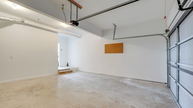 Un garage propre et vide, avec un sol en béton, un panneau en bois sur le mur et une porte de garage en métal.