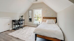 Une chambre à coucher comprenant un lit, un bureau, une chaise et une fenêtre avec des stores.