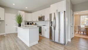 Une cuisine moderne avec des meubles blancs, un réfrigérateur en acier inoxydable et un îlot central agrémenté d’une plante en pot.