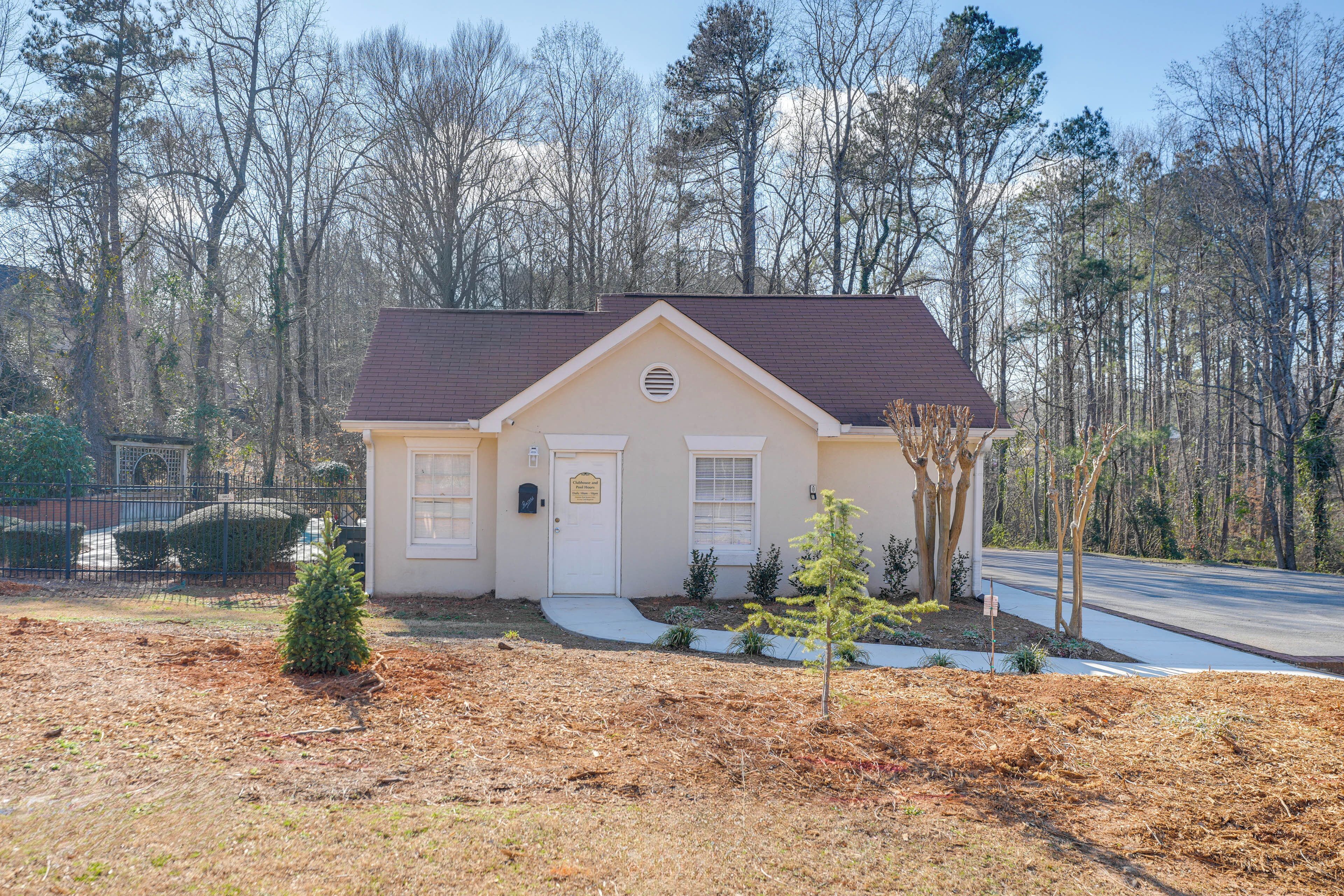 A single-story house with a brown roof, a front door, and a small front yard with a tree and shrubs.