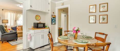 A dining area with a round table, chairs, and a kitchen in the background.