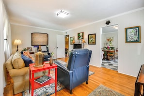 A living room with a sofa, a red side table, a blue armchair, and a dining area in the background. - Near Horse Shows & Events! Blissful Tryon Cottage (Tryon)