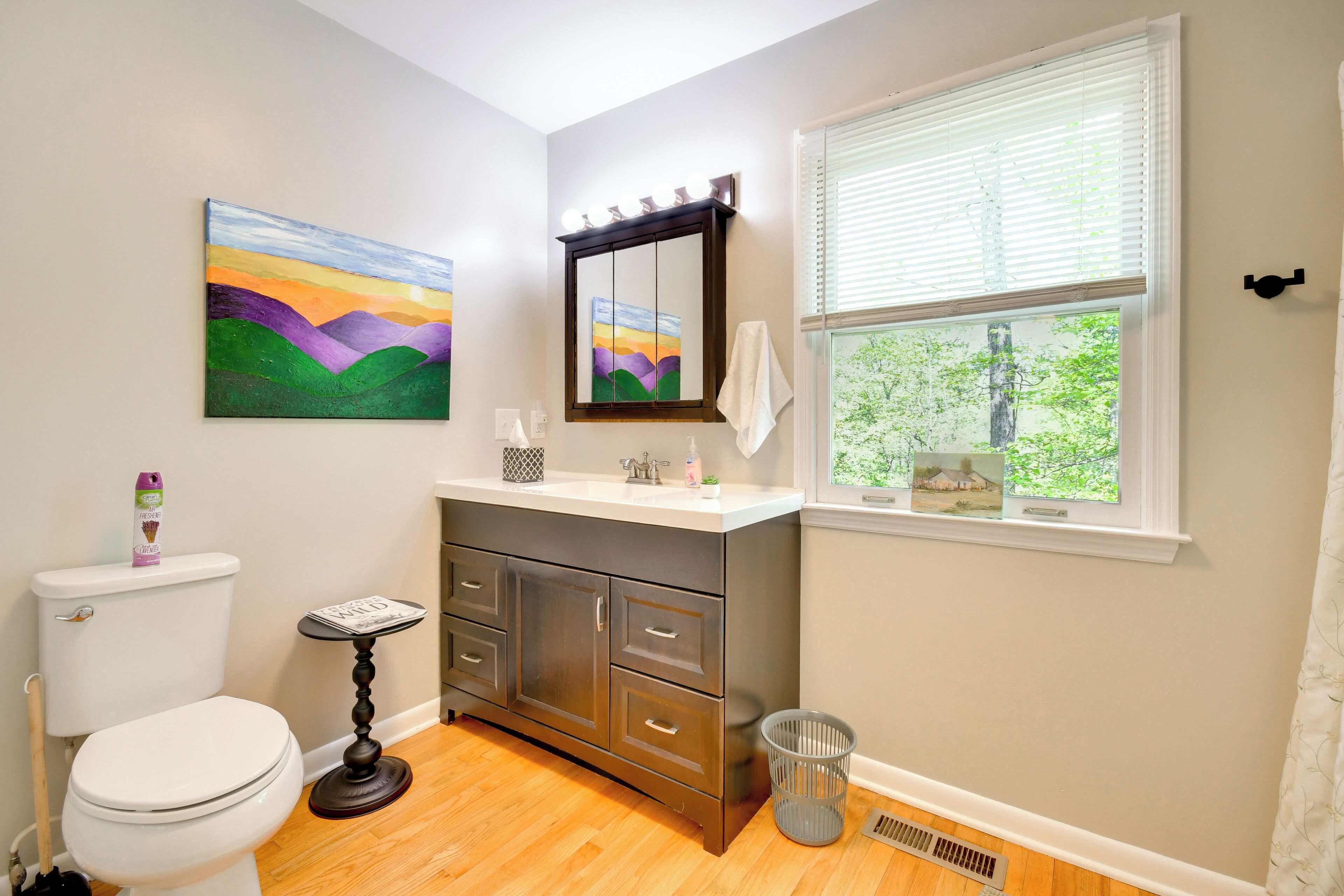 A bathroom with a toilet, vanity, mirror, and window.