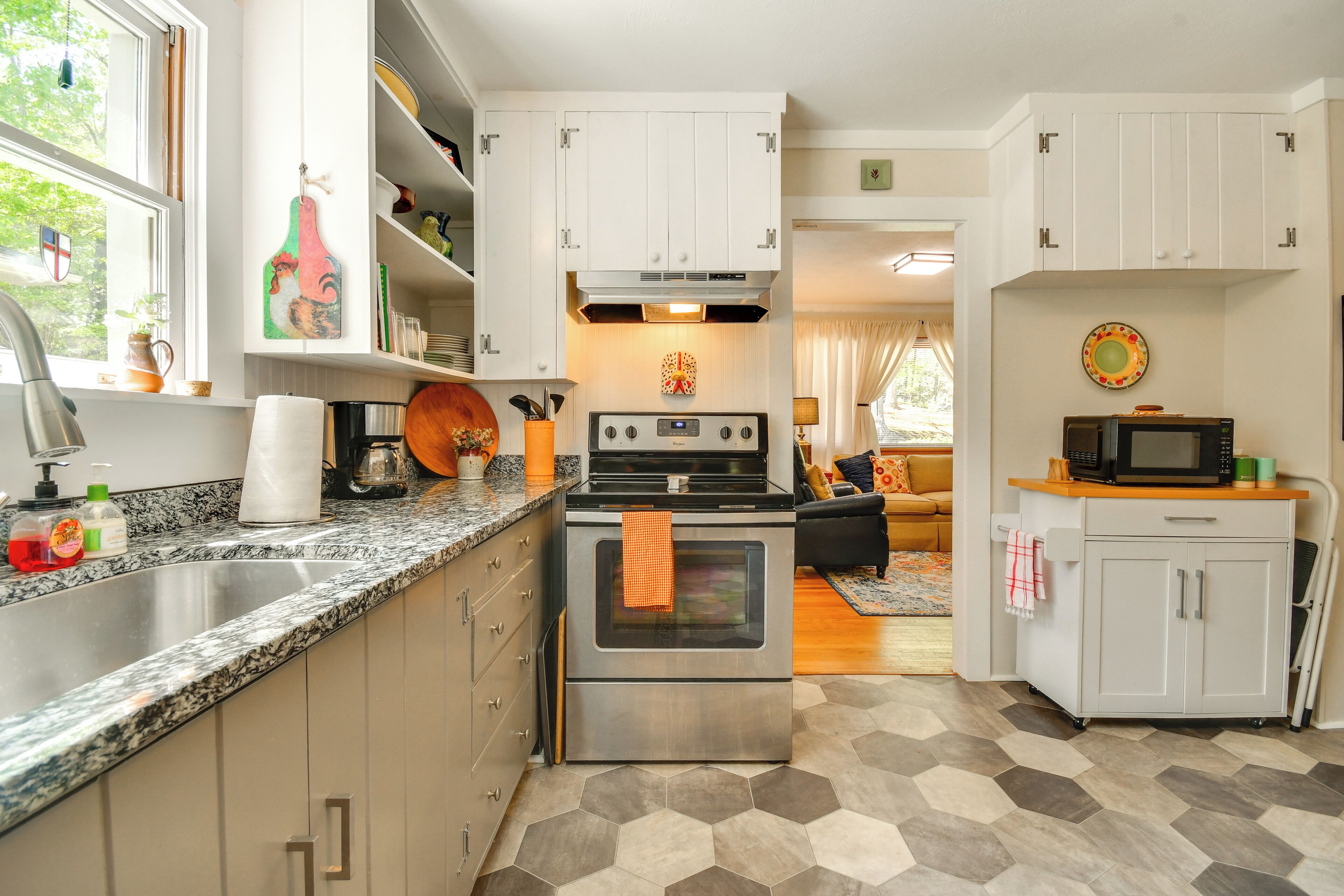 A kitchen with a stainless steel stove, white cabinets, a microwave, and a hexagonal patterned floor.