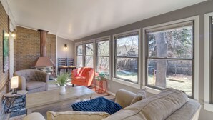 Un salon doté d’une cheminée, de grandes fenêtres et donnant sur le jardin arrière.