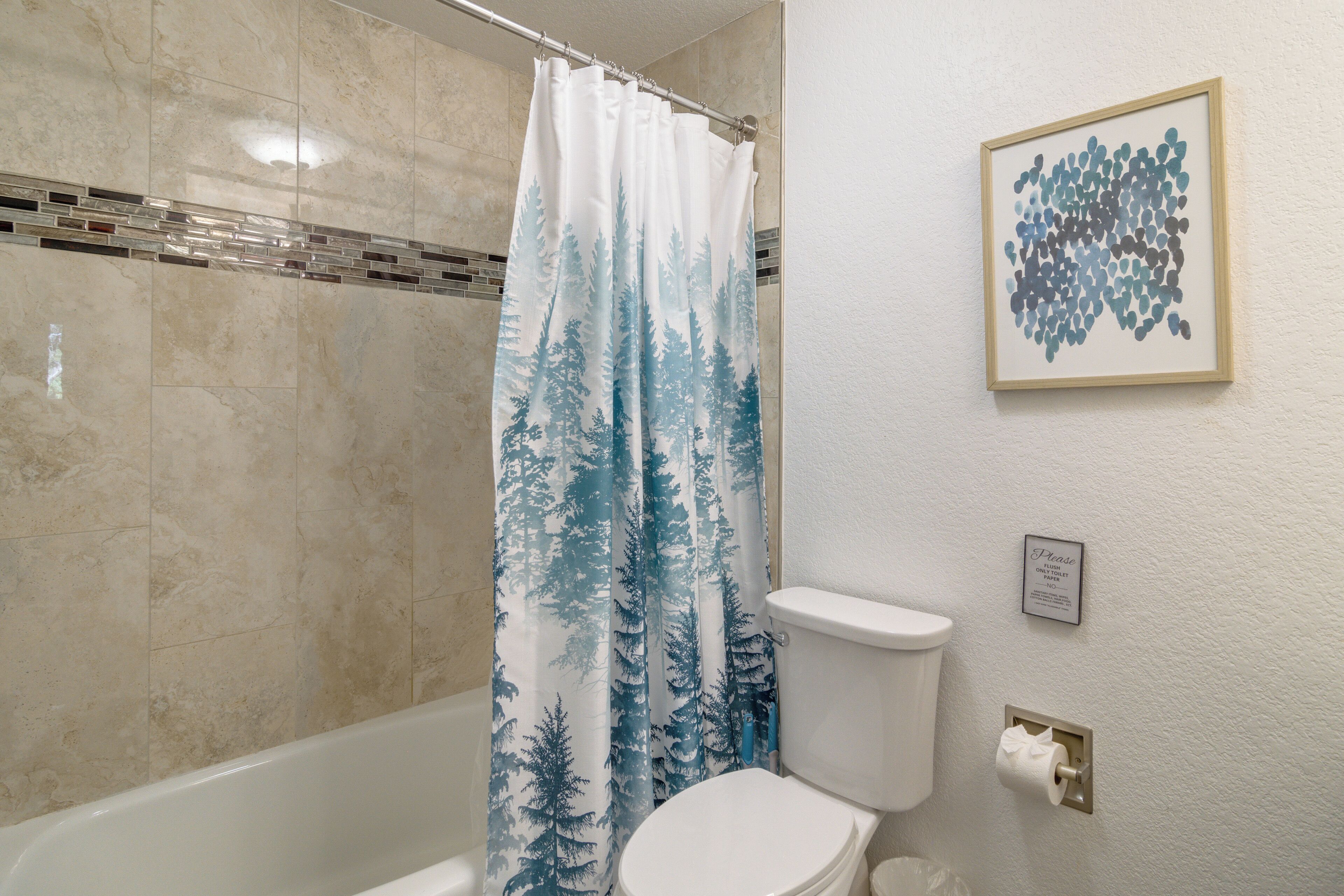 A bathroom with a shower curtain, toilet, and a framed picture on the wall.