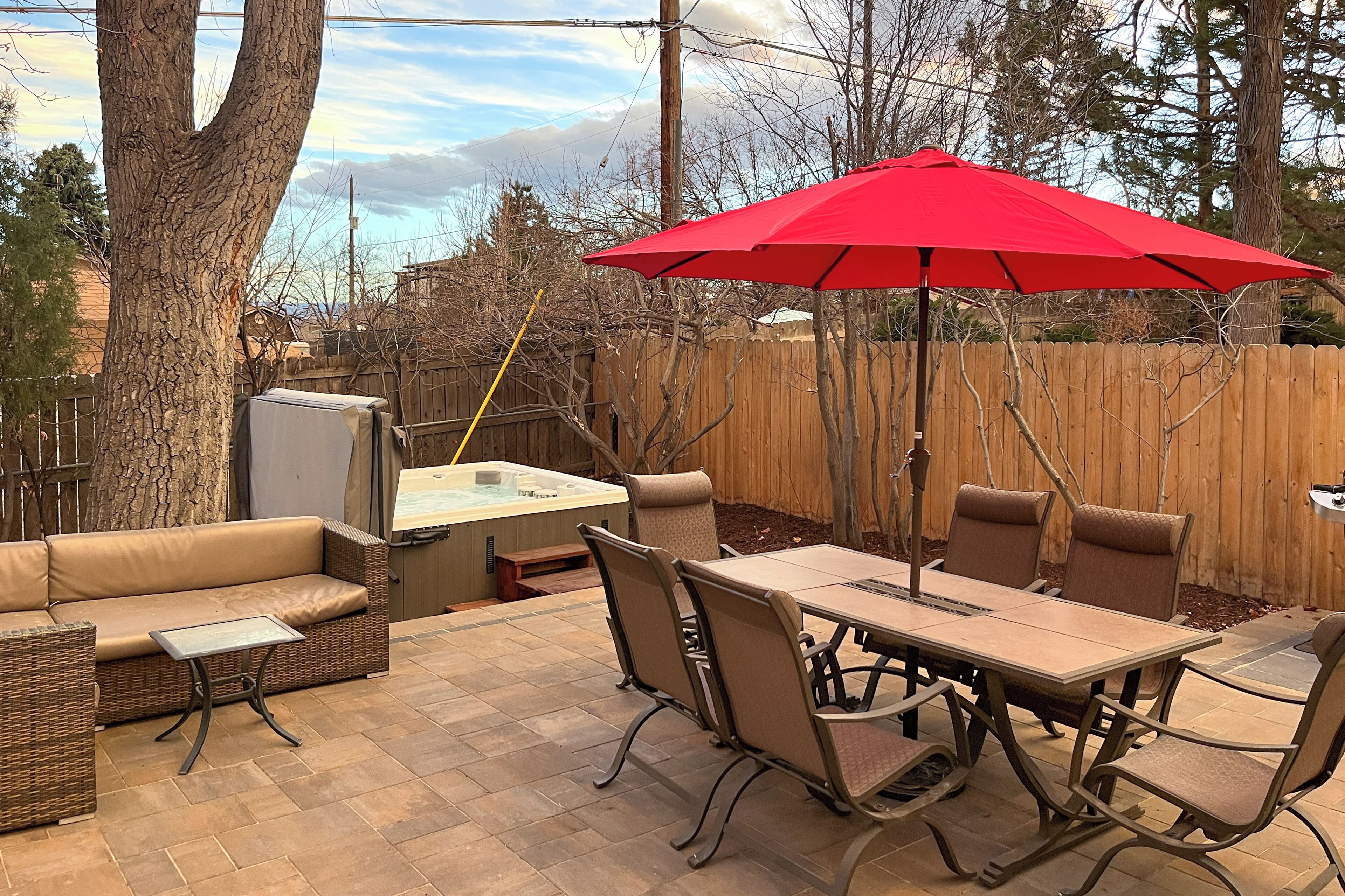 Un patio exterior con mesa, sillas, un paraguas rojo, un sofá y un jacuzzi.