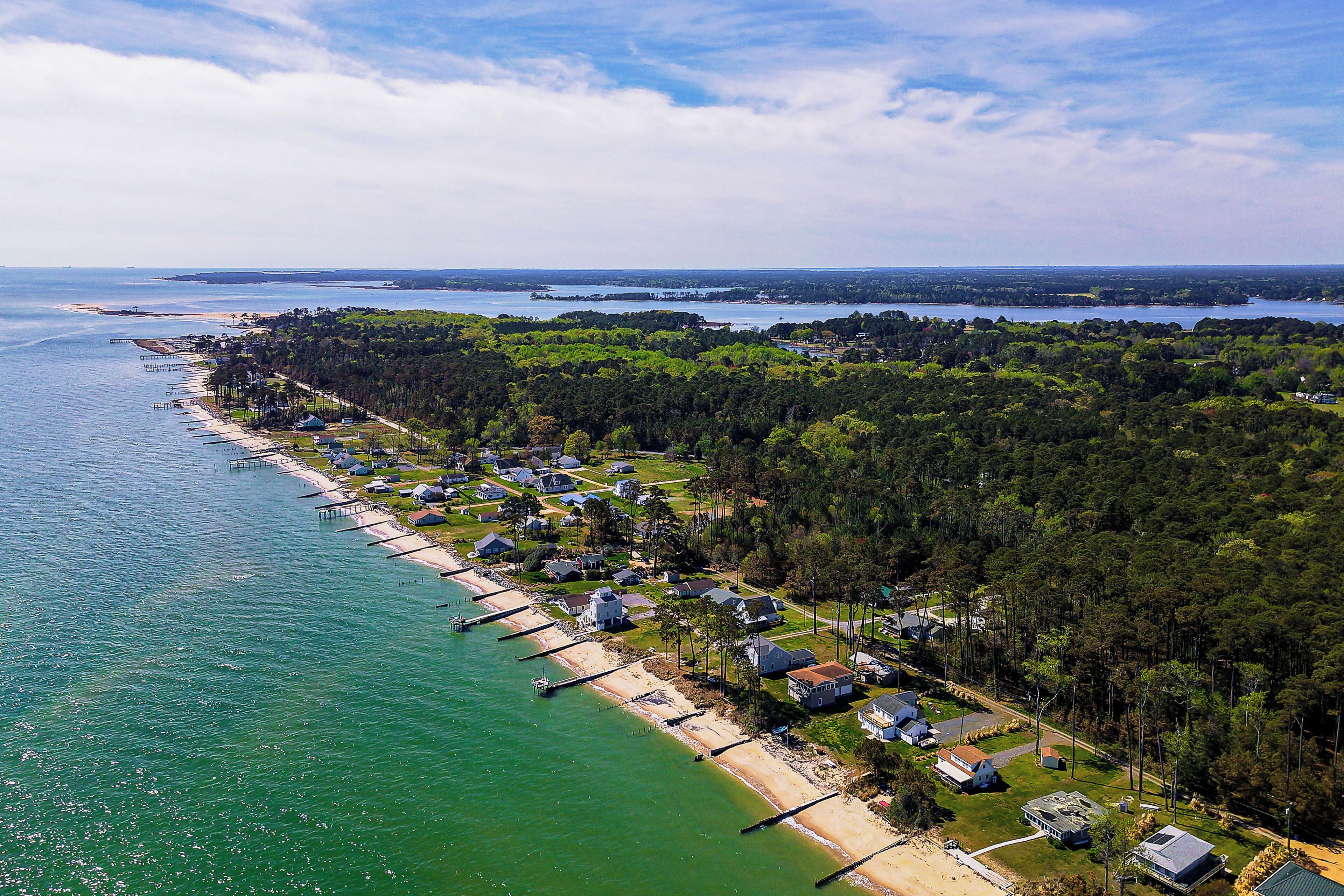 An aerial view of a coastal residential area with houses, a beach, and a pier.
