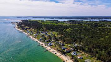 An aerial view of a coastal residential area with houses, a beach, and a pier.