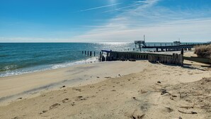 A beach with a wooden pier extending into the water, clear skies, and footprints on the sand. - Gwynn's Island Gem Private Beach & Bay Views (Gwynn)