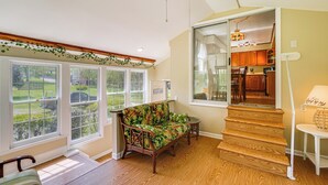 Une pièce spacieuse avec de grandes fenêtres, un escalier en bois, un canapé en osier et une vue sur l’extérieur.