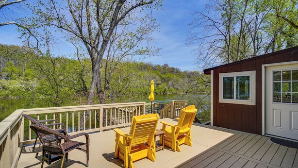 Une terrasse dotée de mobilier d’extérieur, d’une porte et offrant une vue sur un lac entouré d’arbres.