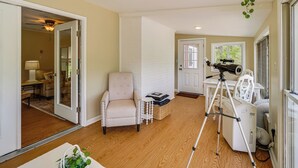 Une pièce avec un plancher en bois, une chaise blanche, un télescope et une porte qui donne sur une autre pièce.