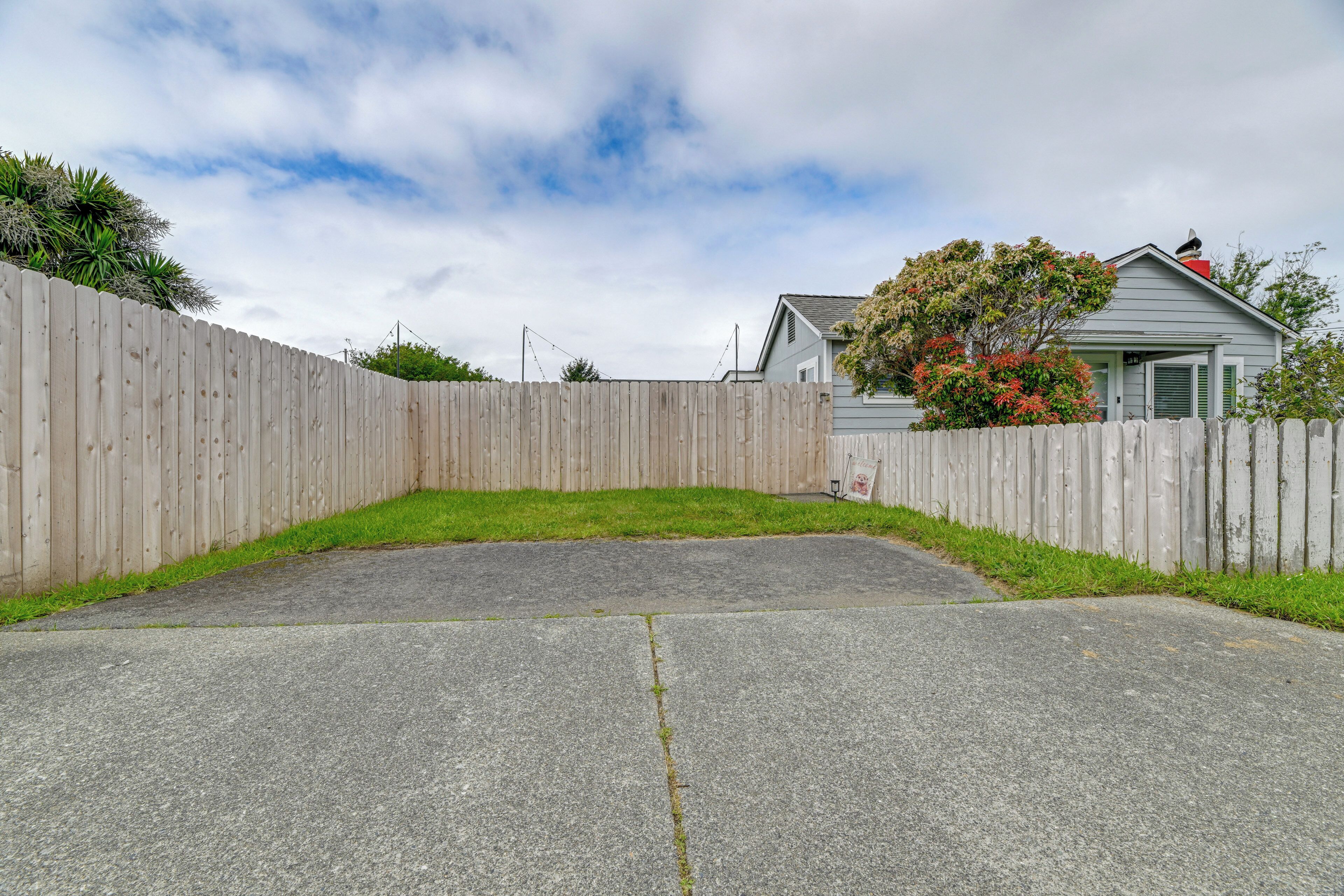 A fenced backyard with a concrete patio, a wooden fence, and a house with green shutters.